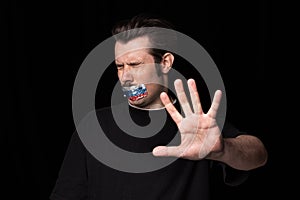Conceptual portrait of young man with three colors duct tape over his mouth isolated on dark background. Censorship