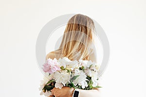 Conceptual portrait of young naked woman with blonde hair with bouquet of white peonies on beige background with copy