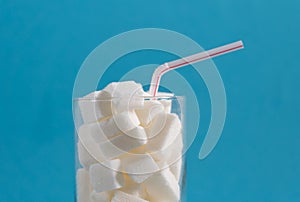 Conceptual still life image of glass full of sugar cubes and straw in excess of calories in soft drinks photo