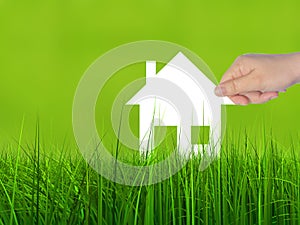 Conceptual white paper house symbol held in hand in green grass