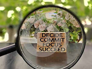 conceptual words of decide commit focus succeed on wooden blocks with magnifying glass background