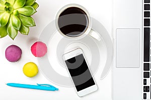 Conceptual workspace or business concept. Green plant in a pot, cup of coffee, colorful macaroons, blue pen, laptop and modern mob