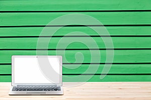Conceptual workspace or business concept. Laptop computer with blank white screen on light wooden table against green wooden wall