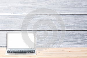 Conceptual workspace or business concept. Laptop computer with blank white screen on light wooden table against grey wooden wall o