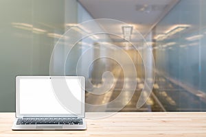 Conceptual workspace or business concept. Laptop computer with blank white screen on light wooden table against modern office inte