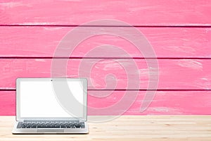 Conceptual workspace or business concept. Laptop computer with blank white screen on light wooden table against painted pink woode