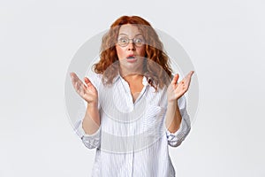 Concerned and ambushed redhead female in glasses, middle-aged woman react to shocking news, raising hands up and gasping