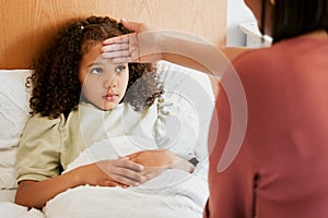 Concerned, anxious and unwell girl suffering with cold or flu while her mother checks her temperature at home. Worried