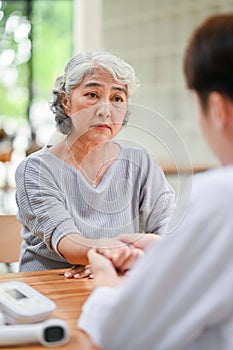 A concerned Asian retired old lady is being diagnosed and checked for pulse on her wrist by a doctor