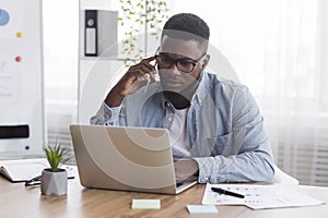 Concerned black employee talking on cellphone and looking at laptop screen