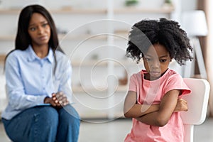 Concerned black woman psychologist looking at angry little girl