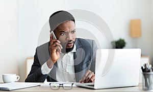 Concerned businessman talking on cellphone and looking at laptop screen