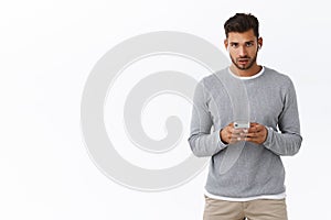 Concerned or busy good-looking bearded guy in grey sweater waiting important business call, holding smartpone look