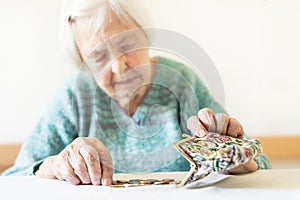Concerned elderly woman sitting at the table counting money in her wallet.