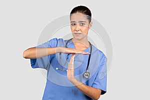 Concerned european nurse in blue scrubs making a timeout sign with her hands, indicating a need for a pause