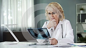 Concerned female pulmonologist examining X-ray of patient's lungs, diagnostics photo