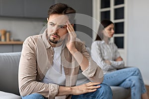 Concerned man with hand on head, distant woman behind