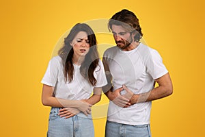 Concerned man and woman with pained expressions holding their stomachs photo