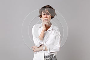 Concerned puzzled young business woman in white shirt posing isolated on grey wall background studio portrait