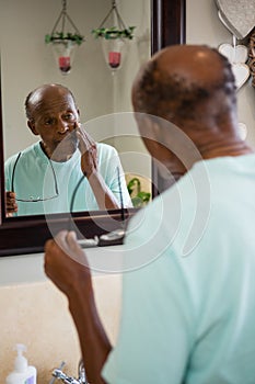 Concerned senior man touching cheek while looking into mirror