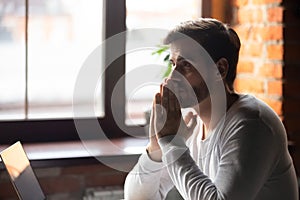 Concerned serious doubtful man sitting near laptop and thinking