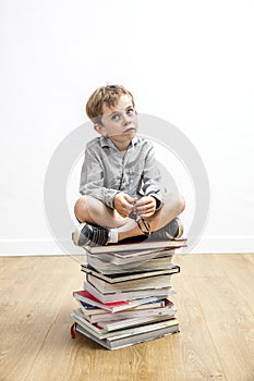 Concerned small gifted kid sitting on books for school learning