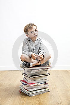 Concerned small gifted kid sitting on books for school learning photo