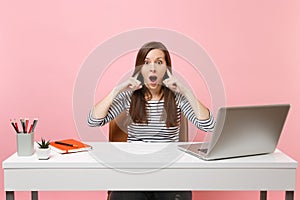 Concerned woman does not want to listen covering ears with fingers sit and work at white desk with contemporary pc