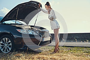 Concerned woman opening car hood and looking inside