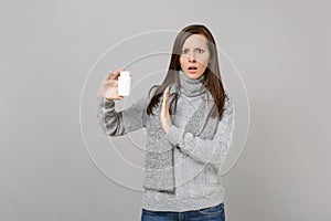 Concerned woman in scarf showing stop gesture with palm to medication tablets, aspirin pills in bottle isolated on grey