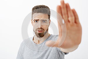 Concerned and worried handsome young male friend with blue eyes, beard and moustache pulling palm towards camera to warn