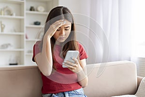 Concerned young asian woman touching forehead while reading message on mobile phone