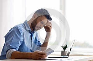 Concerned young businessman looking at smartphone while working in office, waiting message