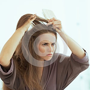 Concerned young woman combing hair in bathroom