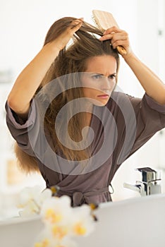 Concerned young woman combing hair in bathroom