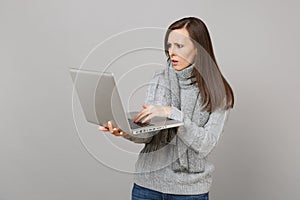 Concerned young woman in gray sweater, scarf working on laptop pc computer isolated on grey wall background. Healthy