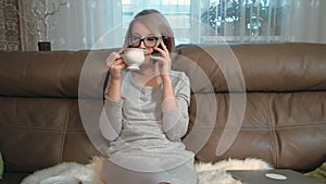Concerned young woman has a phone conversation and drinking tea