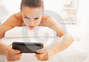 Concerned young woman reading sms while laying on massage table