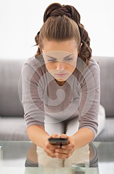 Concerned young woman witn cell phone in hands sitting on couch