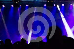 Concert crowd attending a concert, people silhouettes are visible, backlit by stage blue lights. Smart phones are visible here