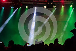 Concert crowd attending a concert, people silhouettes are visible, backlit by stage lights. Raised hands and smart phones are visi