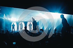 Concert crowd in bright yellow rays. Person lifts a hand with a camera.