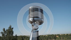 Concert retro vintage microphone on nature. Close up shot of nice and shiny grey microphone. Nice blue sky on background