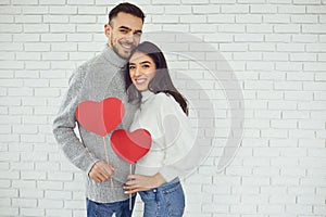Concert Valentine`s Day. Young couple with hearts in hands on a white brick background