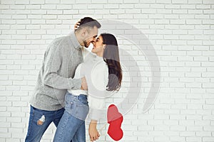 Concert Valentine`s Day. Young couple kissing with hearts in hands on a white brick background