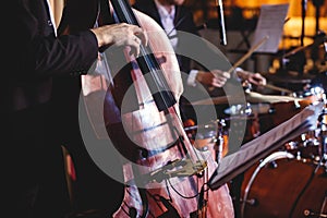 Concert view of a contrabass violoncello player with vocalist and musical during jazz orchestra band performing music,