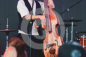 Concert view of a contrabass violoncello player with vocalist and musical rock band during jazz orchestra band performing music,
