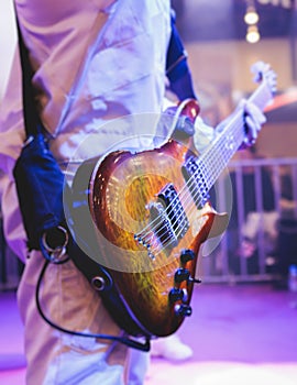 Concert view of an electric guitar player with vocalist and rock band performing in a club, male musician guitarist on stage with