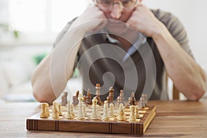 Concetrated man in front of a chessboard in a bright living room at home