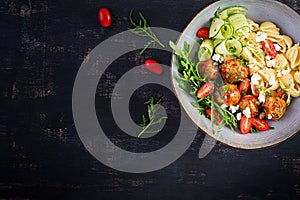 Conchiglie with meatballs, feta cheese and salad on dark background